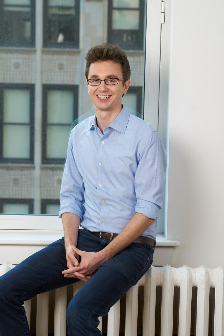 Christopher smiles at camera, poses on a windowsill.