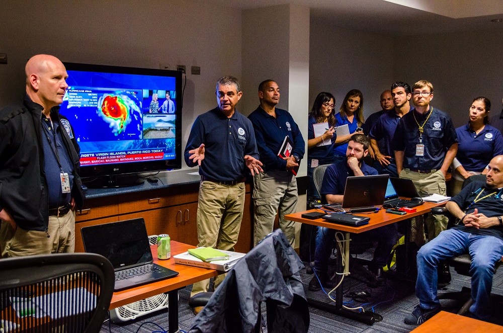 Room packed with FEMA employees watching a hurricane report on TV